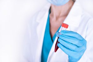 Lekarka w białym fartuchu trzyma w dłoni fiolkę z pobraną krwią pacjenta do analizy i dalszej diagnostyki.