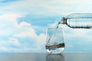 Nalewanie wody do szklanki z plastikowej butelki na tle błękitnego nieba i chmur.. /Źródło: 123rf.com