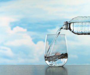 Nalewanie wody do szklanki z plastikowej butelki na tle błękitnego nieba i chmur.. /Źródło: 123rf.com
