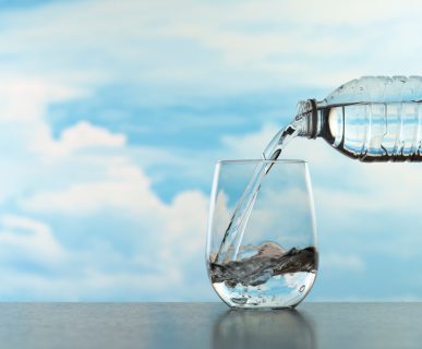 Nalewanie wody do szklanki z plastikowej butelki na tle błękitnego nieba i chmur.. /Źródło: 123rf.com