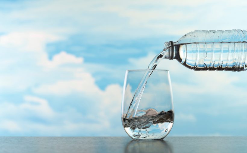 Nalewanie wody do szklanki z plastikowej butelki na tle błękitnego nieba i chmur.. /Źródło: 123rf.com