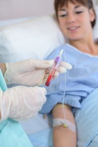 Pobranie próbki krwi z żyły u ręki pacjentki leżącej do fiolki przez pielęgniarkę.