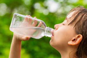 Dziecko pije wodę z butelki, aby się nawodnić i ochłodzić w czasie upału. /Źródło: 123rf.com