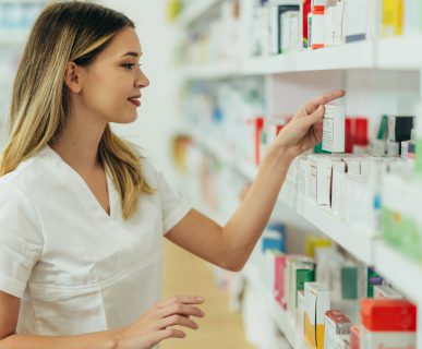 Młoda farmaceutka układa leki na półce w aptece. /Źródło: 123rf.com