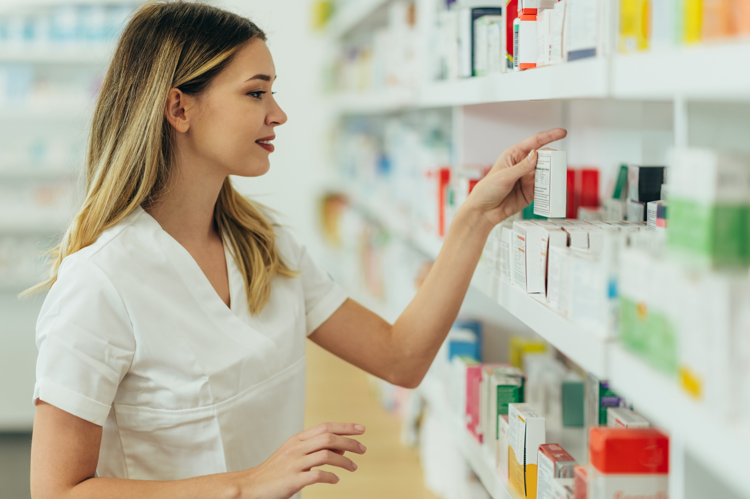 Młoda farmaceutka układa leki na półce w aptece. /Źródło: 123rf.com