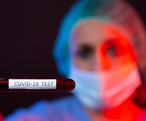 Pielęgniarka w sterylnym stroju trzyma w dłoniach fiolkę z próbką krwi. /Źródło: 123rf.com