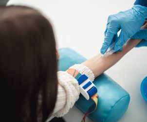 Professional laboratory investigations in healthcare system. Back side top view portrait of female child in process of having haemanalysis in medical office