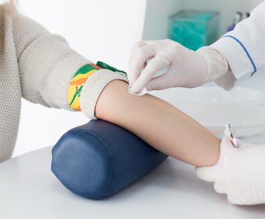 Preparation for blood test with beautiful young blond woman by female doctor in white coat medical uniform on the table in white bright room. Nurse rubbing a hand styryl patient tissue.
