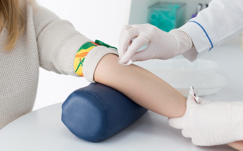 Preparation for blood test with beautiful young blond woman by female doctor in white coat medical uniform on the table in white bright room. Nurse rubbing a hand styryl patient tissue.